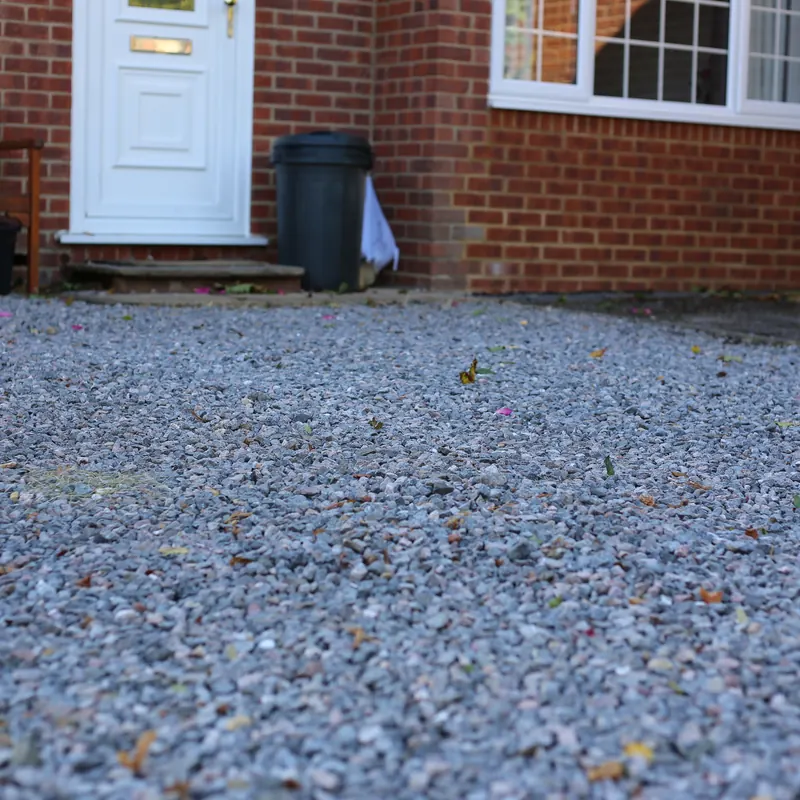Grey gravel driveway in front of a brick house